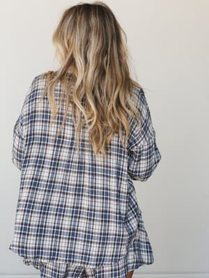 A back-facing shot of a model in a relaxed plaid flannel top — the kind of set that makes staying in feel like a whole personality.