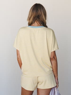 A back-facing shot of a matching stripe tee and shorts set in buttery yellow with white pinstripes and a soft blue contrast collar — the kind of set that makes doing nothing feel intentional.