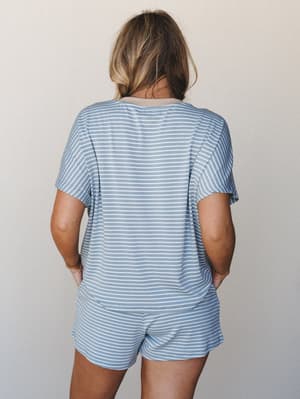 Shot from the back, a matching striped tee-and-shorts set in soft denim blue and cream gives off that easy Sunday morning energy — the kind of outfit you wear to make coffee and somehow never change out of.