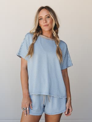 A relaxed matching stripe set — oversized tee and drawstring shorts in soft denim blue — styled with double braids and stacked rings for that effortless, cozy-cool vibe.