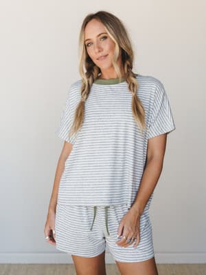 A relaxed striped matching set — oversized tee and drawstring shorts in heather grey with soft olive contrast trim — worn with braided pigtails and stacked rings for an effortlessly comfy, put-together feel.