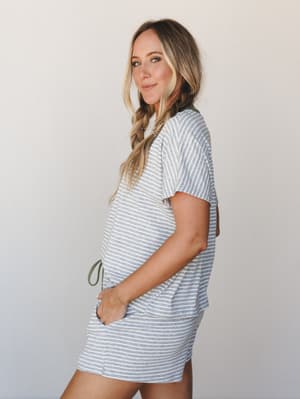 A relaxed side-profile shot of a model in a heather grey striped tee and matching mini shorts with an olive green drawstring — the kind of easy, lived-in set that blurs the line between pajamas and a really good Saturday outfit.