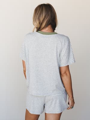 Shot from behind, a model wears a matching striped tee-and-shorts set in heather grey with a soft olive contrast neckline — the kind of effortless two-piece that blurs the line between staying in and stepping out.