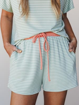 A close-up of a matching striped set in soft mint and white, styled with a coral drawstring waistband that adds just enough color contrast to make it feel intentional — cozy and put-together all at once.