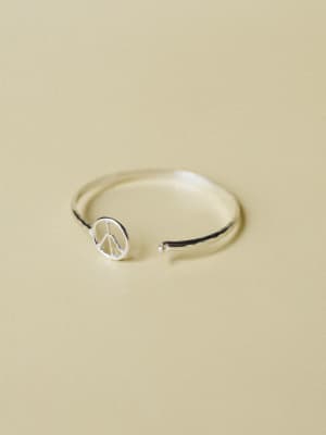 A dainty silver open-cuff ring with a small peace sign charm, shot close-up against a warm sandy backdrop — simple, symbolic, and the kind of thing you'd wear every single day without thinking about it.