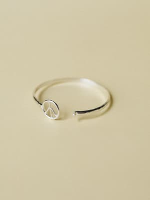 A dainty silver open-cuff ring with a small peace sign charm, shot close-up against a warm sandy backdrop — simple, symbolic, and the kind of thing you'd wear every single day without thinking about it.