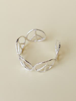 A silver open-cuff bracelet with an intertwined peace sign wire design, shot solo against a warm cream background — the kind of piece that looks like it was found at a market and worn every day since.