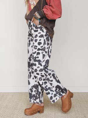 A side-profile shot of wide-leg cow print pants styled with layered tops and studded leather clogs — effortlessly western-boho with a lived-in, mix-and-match energy.