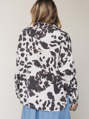 Shot from behind, a model wears an oversized cow print shacket in cream and charcoal over a soft blue midi skirt — the kind of layering piece that feels effortless and a little unexpected.