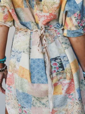 A close-up detail shot of a patchwork-print dress cinched at the waist with a braided lace and leather belt — the kind of effortless, story-rich styling that feels like a quilt your grandmother made and a road trip you're about to take.