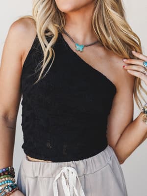 A cropped one-shoulder lace top in black is styled with flowy light gray drawstring shorts, layered boho jewelry, and stacked bracelets — easy, expressive, and totally wearable.