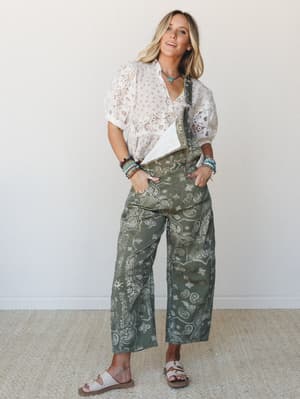 A wide-leg paisley overall in vintage army green is styled over a white eyelet puff-sleeve top, layered with beaded bracelets and a turquoise necklace — the kind of outfit that looks effortless but clearly wasn't an accident.