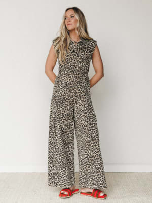 A wide-leg leopard print jumpsuit styled with bold red crochet sandals against a clean white studio wall — effortlessly expressive and ready for wherever the day takes her.
