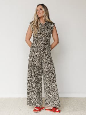 A wide-leg leopard print jumpsuit styled with bold red crochet sandals against a clean white studio wall — effortlessly expressive and ready for wherever the day takes her.