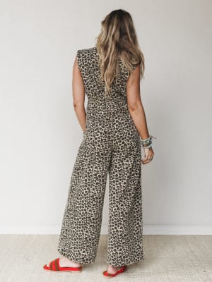 A back-view shot of a wide-leg leopard print denim jumpsuit styled with red crochet sandals and stacked bracelets — the kind of outfit that makes a statement without trying too hard.