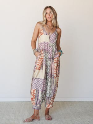 A relaxed patchwork jumpsuit in warm cream and rust tones worn with layered turquoise jewelry and nude sandals — the kind of outfit that looks equally at home at a farmers market or a summer dinner.