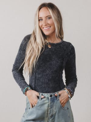 Woman wearing a dark long-sleeve top and light blue jeans with a neutral background