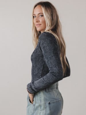 Woman wearing a dark gray sweater and light blue jeans against a plain background