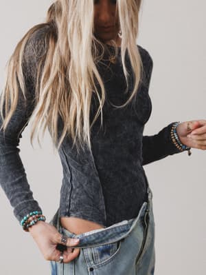 Person wearing a dark ribbed sweater and blue jeans with a neutral background