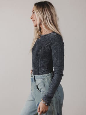Woman wearing a dark long-sleeve top and light blue jeans against a plain background