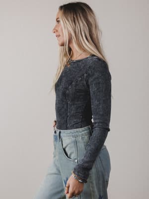 Woman wearing a dark long-sleeve top and light blue jeans against a plain background