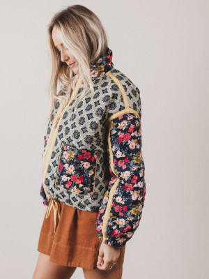 Woman wearing a patterned jacket with floral designs on a plain background