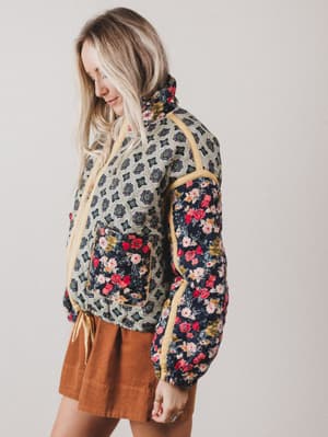 Woman wearing a patterned jacket with floral designs on a plain background