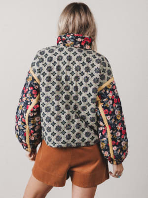 Person wearing a patterned jacket with floral sleeves on a plain background