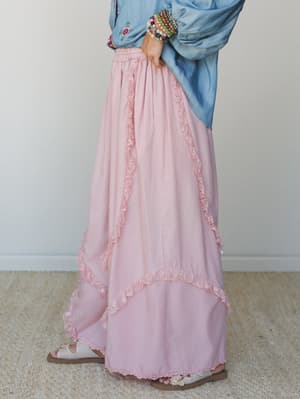 A dreamy blush pink maxi skirt with layered ruffle and lace trim details, styled with a chambray embroidered top and stacked beaded bracelets — soft, romantic, and effortlessly boho.