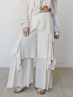 An all-cream boho set styled with wide-leg ruffle pants and a flowy cropped top, shot from the waist down with a turquoise pendant necklace peeking in — soft, romantic, and effortlessly undone.