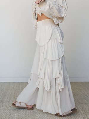 A dreamy cream-on-cream moment — tiered ruffle wide-leg pants paired with a lace-trimmed ruffle top, shot from the side to show off all that movement and layered texture.