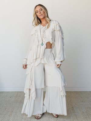 An all-cream, head-to-toe ruffle moment — wide-leg pants with cascading petal tiers paired with a matching ruffled crop top, styled with a turquoise pendant necklace for that effortless boho energy.