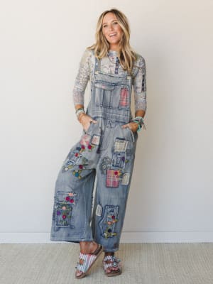 Wide-leg denim overalls covered in mixed patchwork and colorful floral embroidery, styled over a floral mesh long-sleeve top with stacked bracelets and embellished sandals — the kind of outfit that looks like it took zero effort and all of it at once