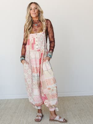 A wide-leg patchwork jumpsuit in soft pink and peach tones styled over a sheer brown lace long-sleeve top, accessorized with stacked beaded bracelets and a turquoise butterfly necklace — effortlessly boho with a laid-back, put-together feel.