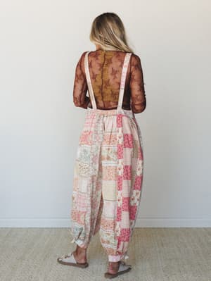 Shot from the back, a model wears a breezy patchwork overalls-style jumpsuit in soft pinks and peach over a sheer lace long-sleeve top — the kind of outfit that looks like it was pulled together effortlessly but very much was not.