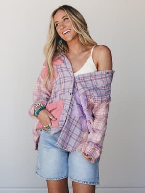 A sun-kissed model laughs off to the side in a pastel plaid flannel shirt worn open over a white lace cami, paired with light wash denim bermuda shorts — the whole look has that easy, thrown-together energy of a really good weekend.