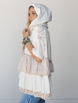 A breezy, texture-rich tiered top with a hooded scarf draped overhead — lace panels, mixed stripe and floral ruffles, and a stack of beaded bracelets give it that perfectly collected, free-spirited feel.