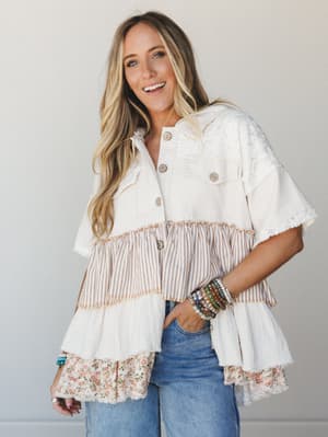 A tiered patchwork top in cream and natural tones — mixing lace, stripes, gauze, and floral trim in a way that feels like it was made from the best parts of every fabric you've ever loved, styled with wide-leg jeans and stacked bracelets for an effor