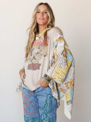A relaxed, expressive look built around a patchwork poncho draped over a graphic tee and embroidered wide-leg jeans — the kind of outfit that looks like it came together effortlessly but absolutely did not.