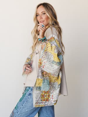 A model styled in a patchwork poncho layered over a graphic tee and embroidered jeans, shot in profile against a soft studio wall — the whole look feels like a well-loved wardrobe that tells a story.