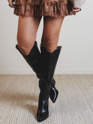 Person wearing black knee-high boots on a neutral background