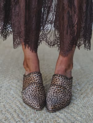 A close-up detail shot pairing leopard-spot haircalf mules with a moody plum lace hem — the kind of styling that makes the shoes the whole personality of the outfit.