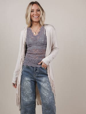 Woman wearing a patterned top, cardigan, and jeans with a beige background