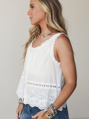 A white eyelet tank top styled with denim and layered beaded bracelets — the kind of top that feels like summer without trying too hard.