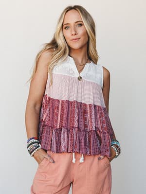 A tiered sleeveless top in mixed boho prints — white lace yoke at the top, blush micro-pattern in the middle, and a deep mauve patchwork print at the hem — styled with peachy linen-look joggers and stacked beaded bracelets for an effortlessly express