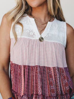 A close-up of a sleeveless tiered boho top with a lace yoke, mixed patchwork prints in mauve and berry, styled with layered gold necklaces and a beaded bracelet — the kind of top that makes a casual afternoon feel a little more intentional.