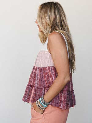 A tiered boho tank top in mixed mauve and burgundy prints is styled with peachy pink jeans and a stack of turquoise and pearl bracelets — the kind of effortless summer look that feels intentional without trying too hard.