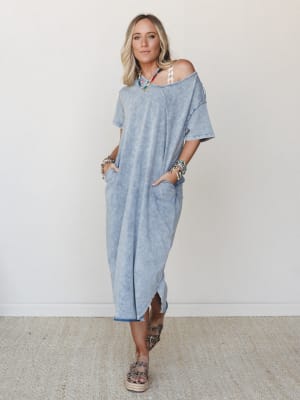An oversized mineral-washed maxi tee dress in a faded denim blue, styled off-the-shoulder with layered boho jewelry and platform sandals — the kind of effortless look that feels like a good day.