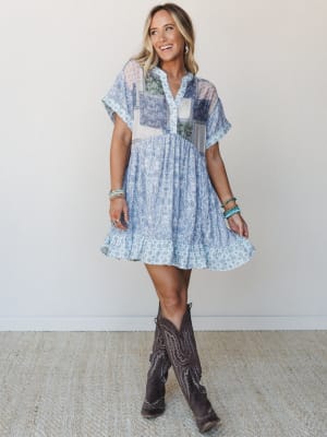 A patchwork mini dress in soft periwinkle and mixed boho prints pairs with tall dark brown cowboy boots and stacked turquoise bracelets — the kind of outfit that looks like it was thrown on effortlessly but absolutely wasn't.