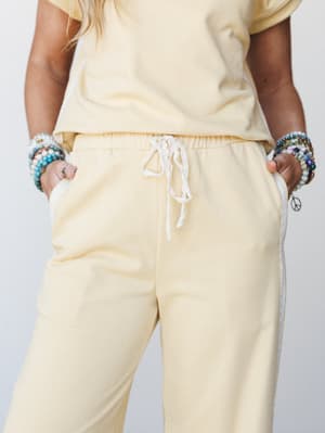 A close-up mid-shot of soft butter-yellow jogger pants styled as a matching set, with a lace drawstring and lace-trim pockets — the kind of outfit that feels like a good morning.
